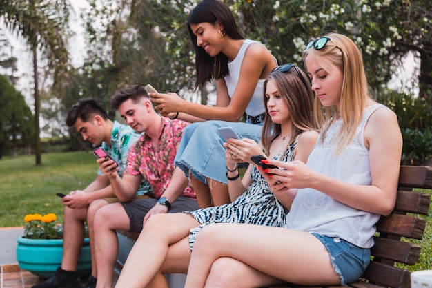 Group of friends sitting in the park. Young millennial friends enjoy technology. Friends checking out their social networks. Concept of friendship, outdoor and technology.