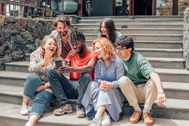 Group of friends sitting on stairs outdoors young people together having fun with mobile phones outside