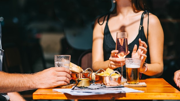 Group of friends sitting on a summer terrace with beer and champagne in their hands and snacks on the table