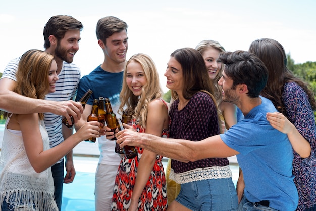 Group of friends toasting beer bottles near pool