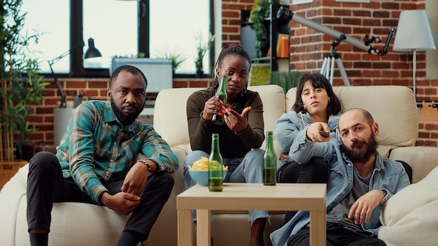 Group of friends watching action movie on tv channel program, drinking beer from bottles. People enjoying leisure activity with drinks and television film or show. Tripod shot.