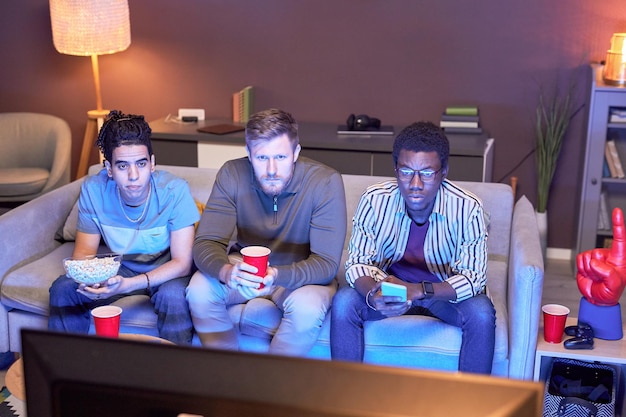 Group of friends watching TV at home and eating snacks lit by blue light