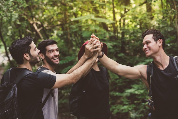 Photo group of friends with backpacks happy fun join hands together while walking adventure travel in forest