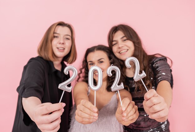 A group of girlfriends on a pink background are holding the numbers 2022, New Years celebration, Christmas party.