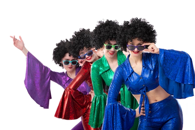 A group of girls in colorful flared suits and afro wigs pose against a white background