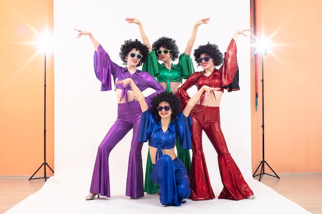 A group of girls in colorful flared suits and afro wigs pose in a photo studio