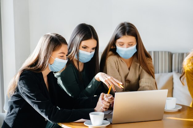 A group of girls in masks sit in a cafe and work on laptops. Teaching students.