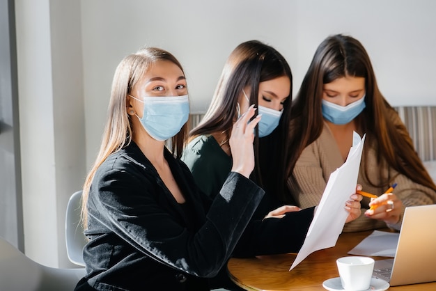 A group of girls in masks sit in a cafe and work on laptops. Teaching students.