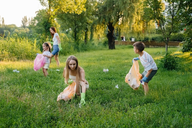 A group of girls with children at sunset are engaged in garbage collection in the park. Environmental care, recycling.