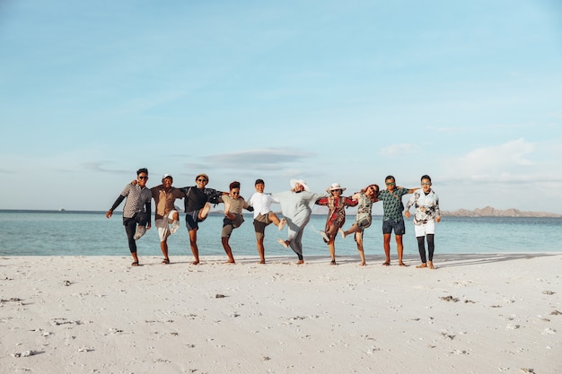 Group of happy Asian friends enjoying vacation with embrace each other and dance on the beach