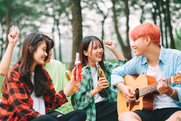 Group of happy Asian young people sitting on the guitar and singing in the park