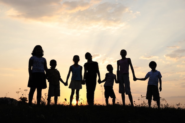 Group of happy children playing on meadow, sunset, summertime