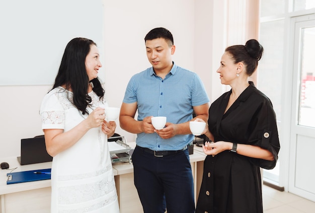 A group of happy colleagues are talking standing at the office window with cups of coffee people in the office