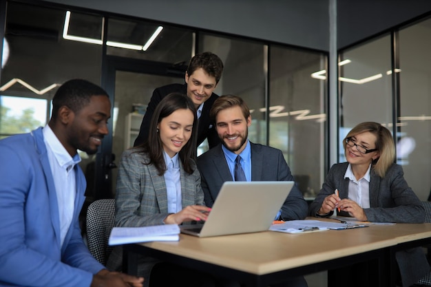 Group of happy diverse male and female business people in formal gathered around laptop computer in bright office.