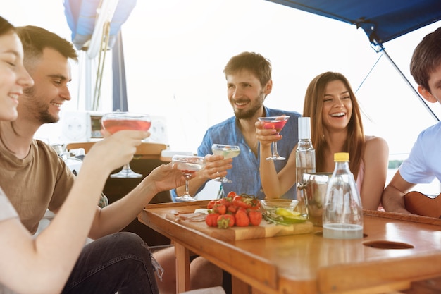 Group of happy friends drinking vodka cocktails at boat party outdoor