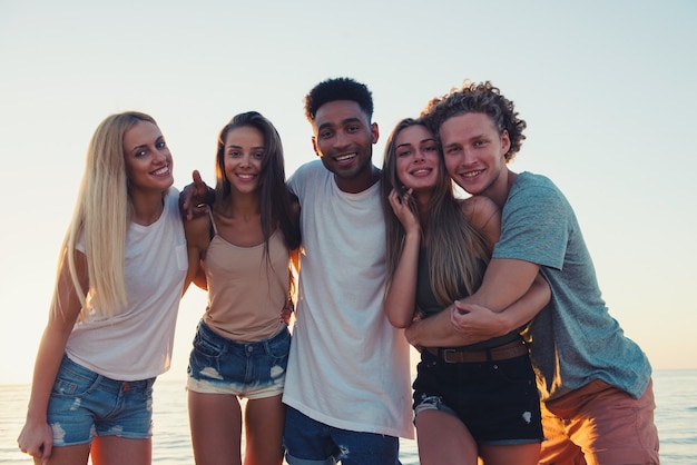 Group of happy friends having fun at ocean beach at dawn