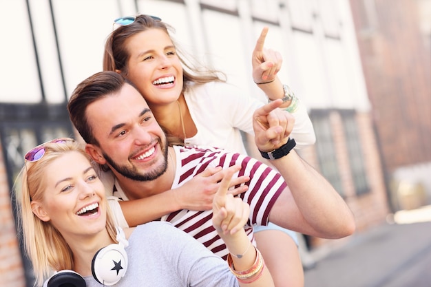 group of happy friends smiling to the camera and pointing at copy space