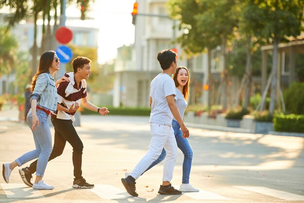 Group of happy laughing young Vietnamese people crossing road on sunny summer day