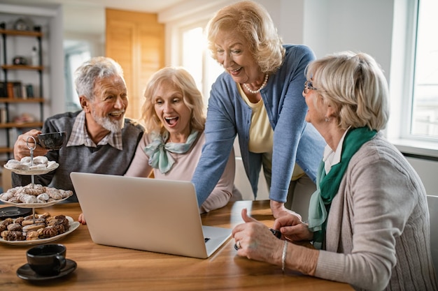 Group of happy mature people having fun while surfing the net on a computer at home