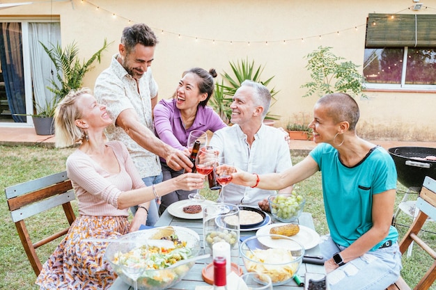 Group of happy middleaged men and women toasting wine glasses at dinner event at house backyard