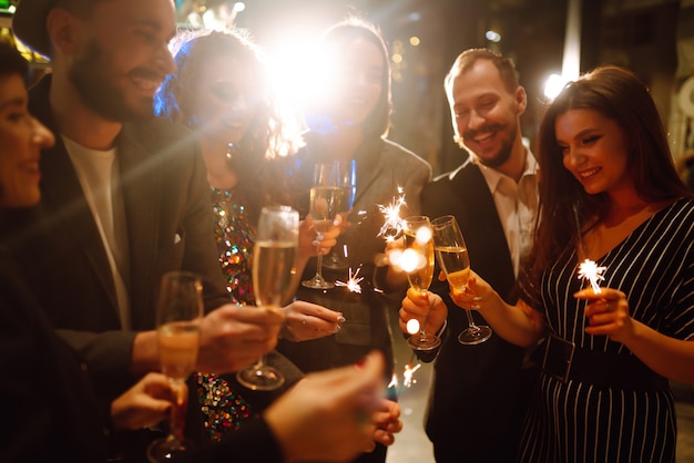 Group of happy people holding sparklers at the party. Young friends clinking glasses of champagne.