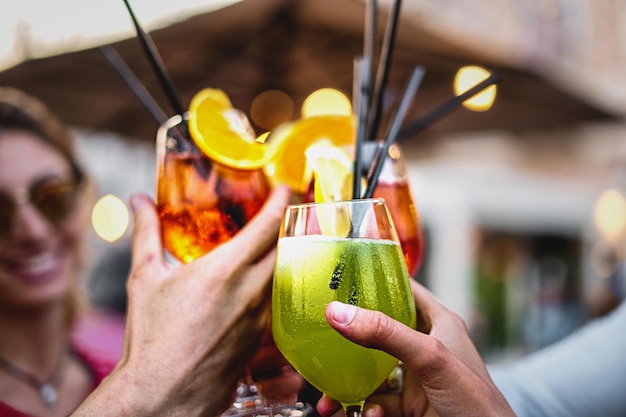 Group of happy people rising cocktail glasses for a celebratory toast friends at restaurant clinking mocktails concept of people meeting on summer closeup shot focus on the green glass