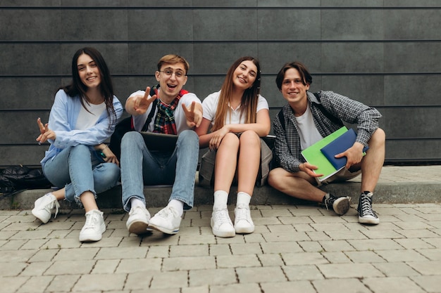 Group of happy smiling students sitting on the floor against dark wall College learning concept