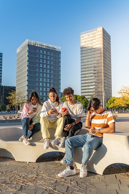 Group of happy teenage friends looking the phones in a bench in the city street