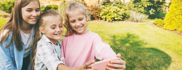 Group of happy teenage girls laughing and taking a selfie on mobile phone outdoors