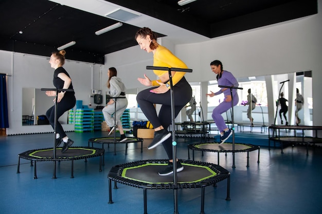 Group of happy women warming up before training in gym jumping on trampoline