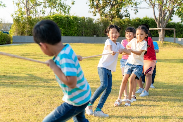 Group of happy young Asian children playing tug of war or pull rope togerther outside in city park playground in summer day. Children and recreation concept.
