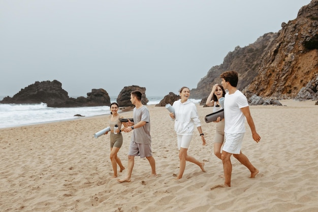 Group of happy young people walking on the beach with yoga mats preparing for fresh workout at