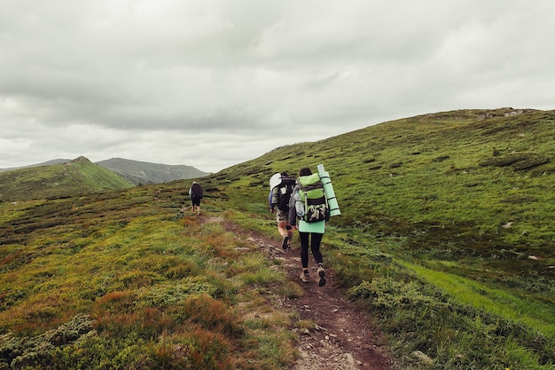 group of hikers with backpacks walk along a trail towards a mountain ridge. 