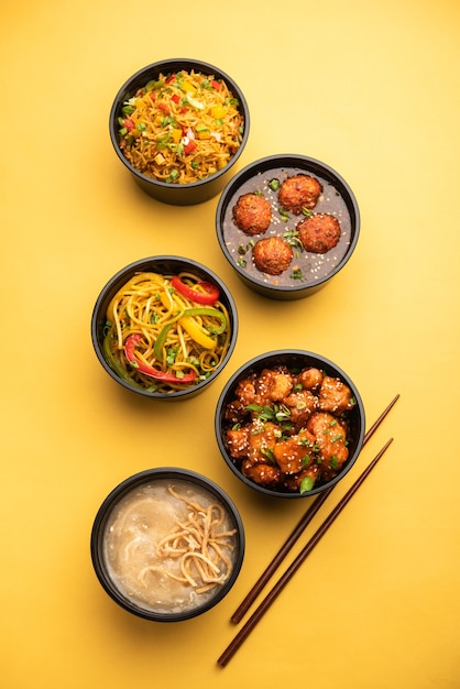 Group of home delivered Indo Chinese food in plastic packages, containers or boxes containing schezwan noodles, fried rice, chilli chicken, manchurian and soup.