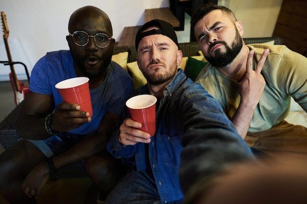 Group of intercultural friends with drinks making selfie in front of camera