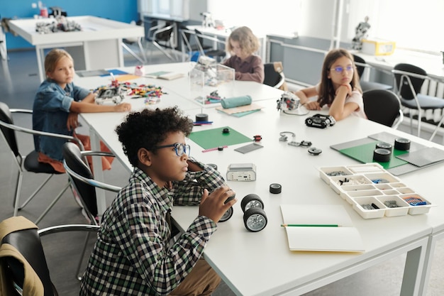 Group of intercultural schoolkids sitting by large desk during presentation