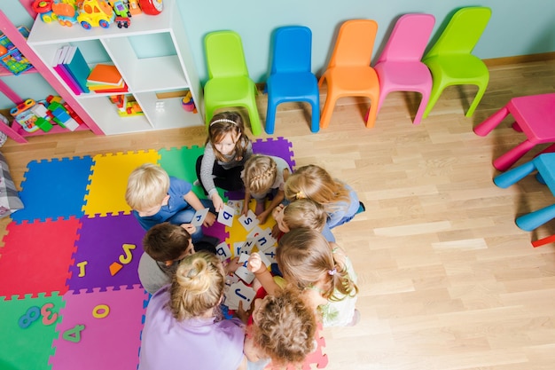 Photo group of kindergarten kids sitting closely on a floor together with teacher providing group work children learning to cooperate while solving tasks