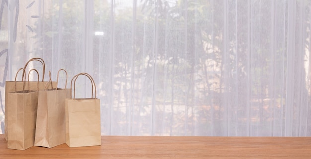 Group of kraft paper bags wit copy space on wood table with white curtain windows.