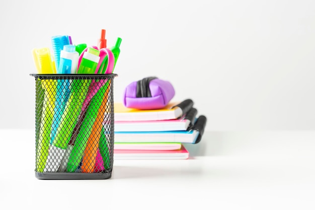 Group of markers colored pens scissors in a metal basket next to several colored notebooks