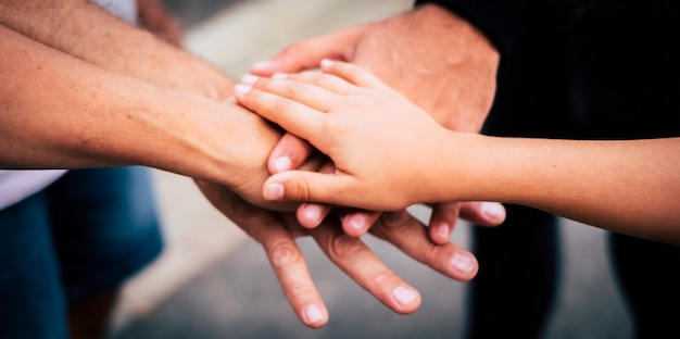 Group of mixed ages people hands together touching and holding like a team concept -  outdoor mixed geneation family and friends putting hands together