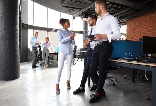 Group of modern business people are talking and smiling while standing in the office hallway.