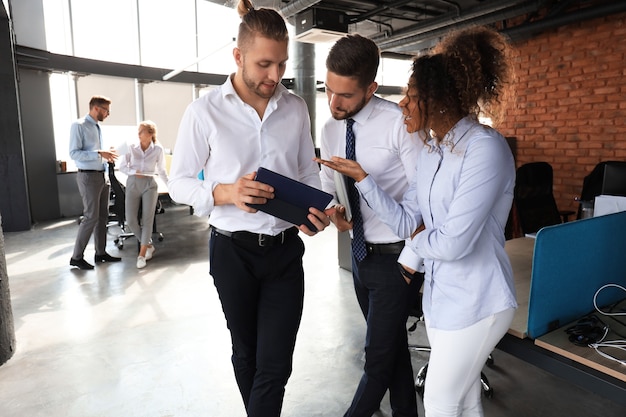 Group of modern business people are talking and smiling while standing in the office hallway.