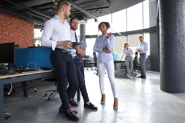 Group of modern business people are talking and smiling while standing in the office hallway.