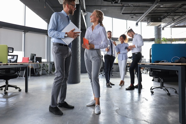 Group of modern business people are talking and smiling while standing in the office hallway.