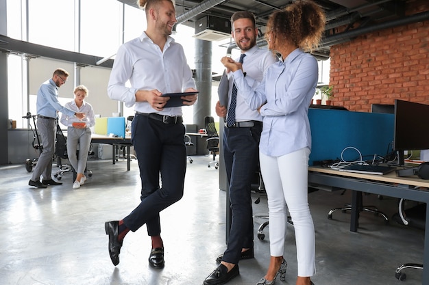 Group of modern business people are talking and smiling while standing in the office hallway.