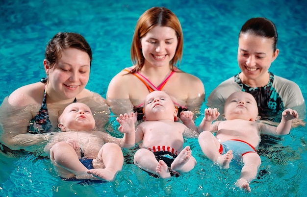 A group of mothers with their young children in a children's swimming class with a coach.