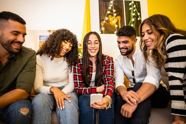 Group of multi ethnic young friends at home sitting on the sofa having fun