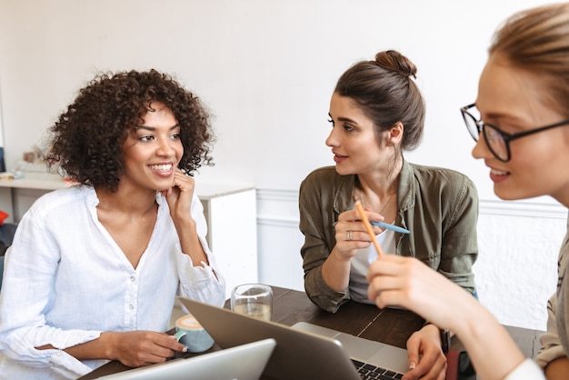 Group of multiethnic cheerful young women studying together at the coffee shop