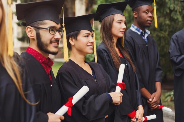 Group of multiethnic students holding their diplomas on graduation day, Happy people celebrating education degree, copy space