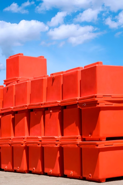 Group of orange foldable ice buckets stack on courtyard outside of storage against blue sky